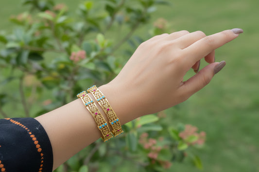 Hand wearing a gold bracelet with colorful stones on a reflective surface
