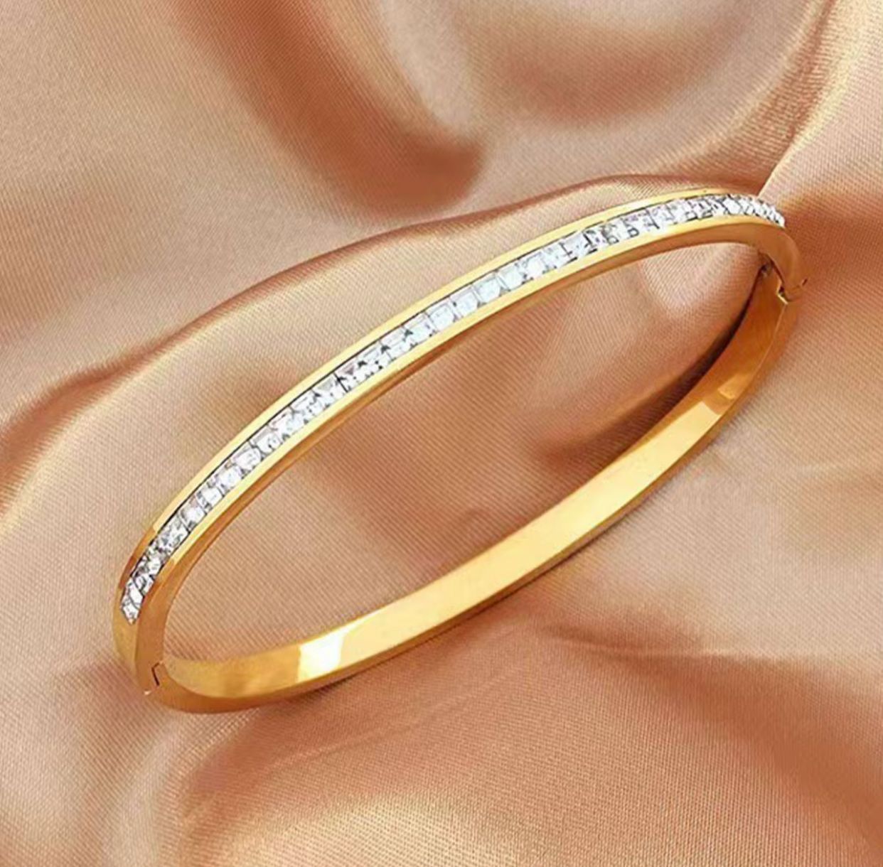 Gold bangle with diamonds on a beige fabric background