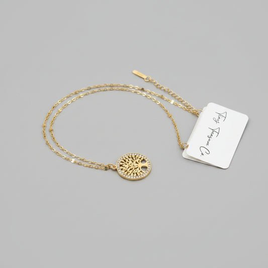 Gold necklace with a circular pendant on a gray surface, accompanied by a tag.