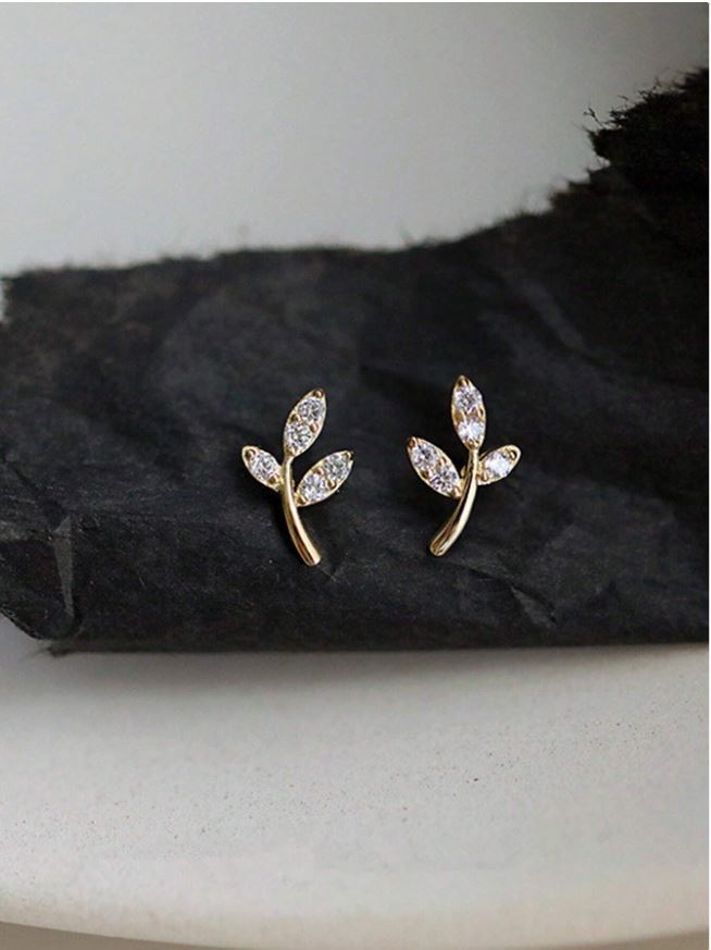 Gold leaf-shaped earrings with clear stones on a dark fabric background