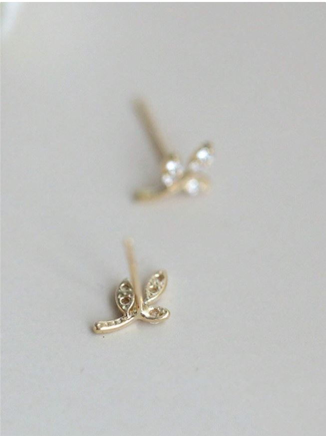 Gold earrings with leaf design on a light gray background