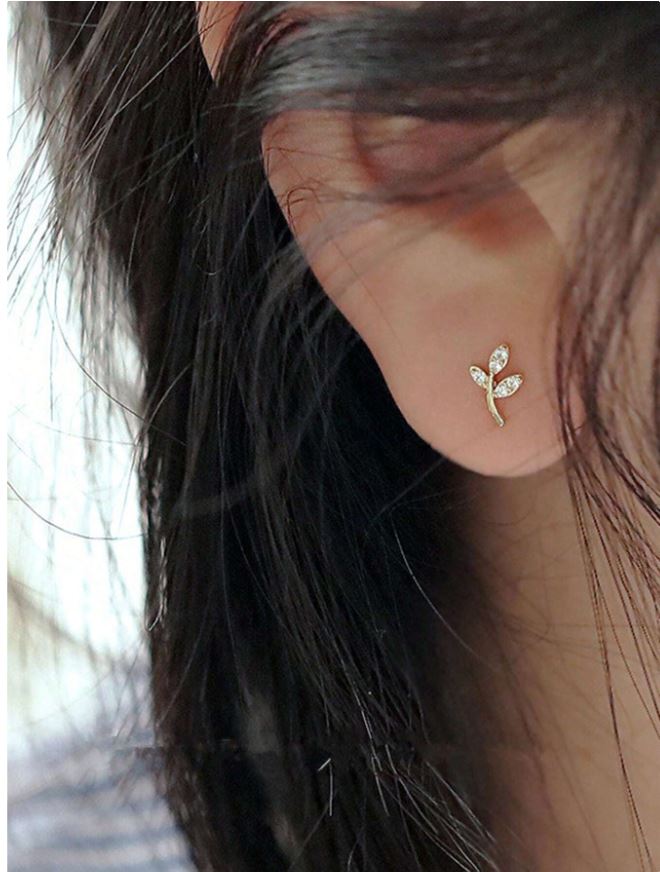Gold leaf-shaped earring worn by a person with blurred background