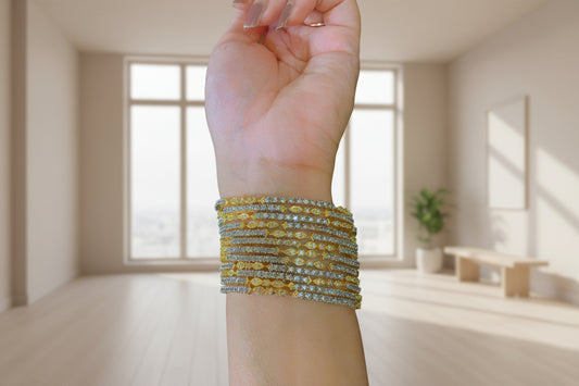 Hand wearing multiple gold and diamond bracelets on a blurred background