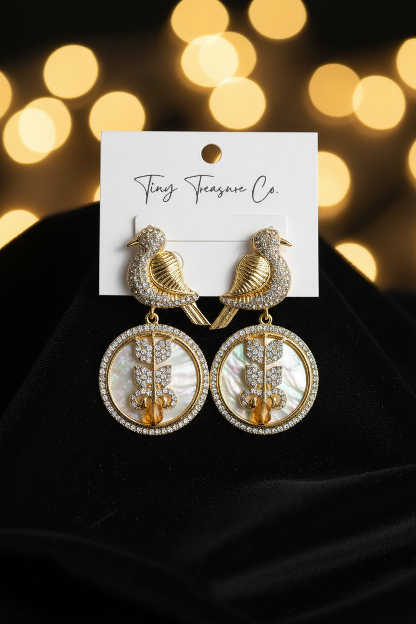 Gold bird-shaped earrings on a Tiny Treasure Co. card held by a hand.