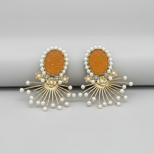 Ornate earrings with pearls held against a blurred background