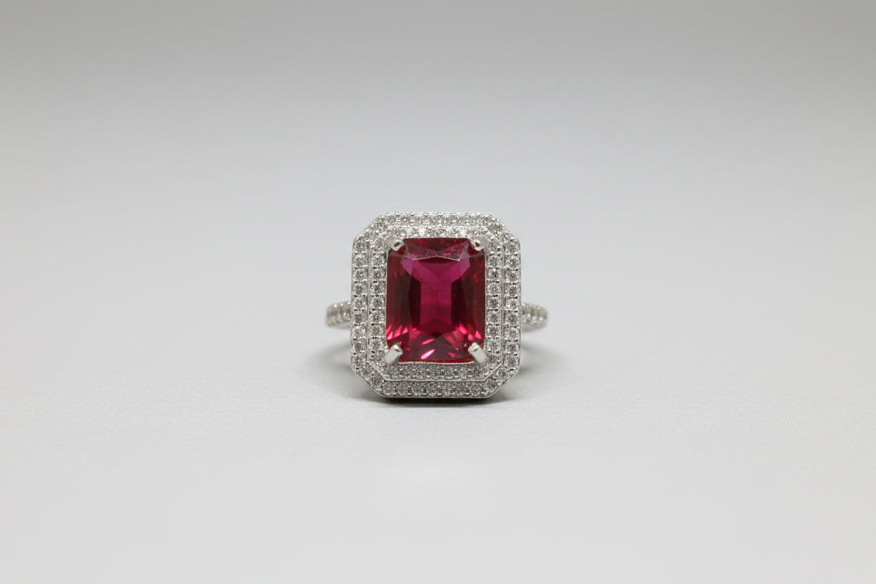 Ring with a red gemstone and silver border on a  white surface