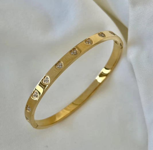 Gold bracelet with heart-shaped diamond accents on a white fabric background