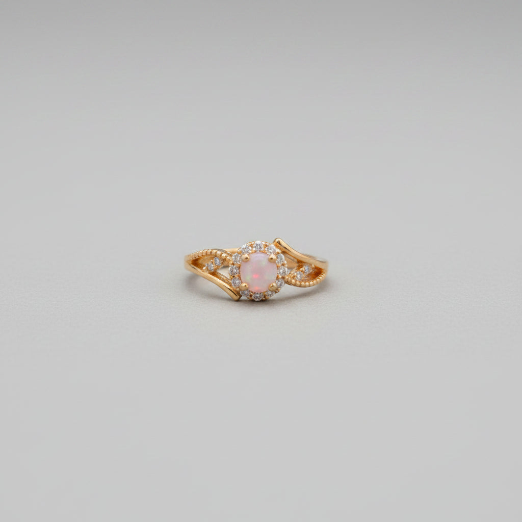 Gold ring with pink gemstone on a reflective surface