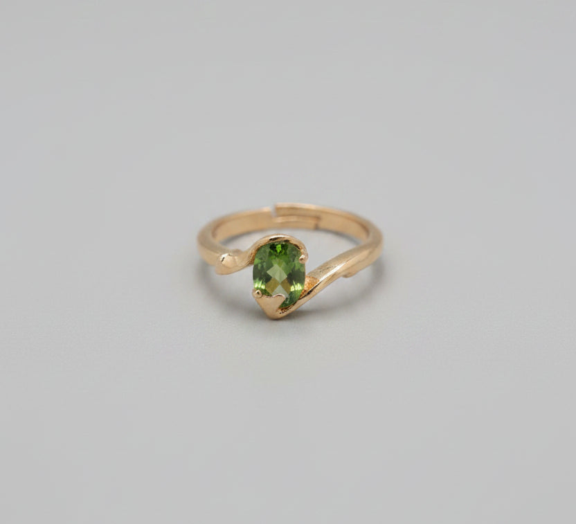 Gold ring with a green gemstone on a reflective surface