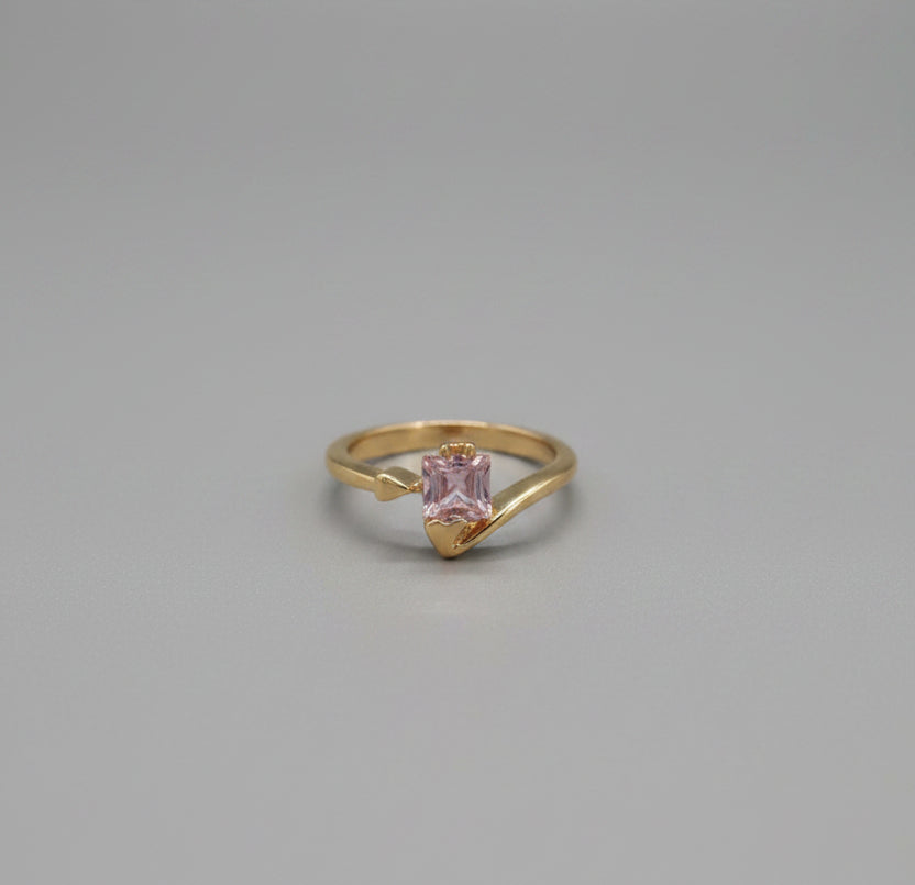 Gold ring with a pink gemstone on a reflective surface