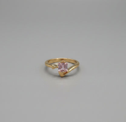 Gold ring with a pink gemstone on a reflective surface