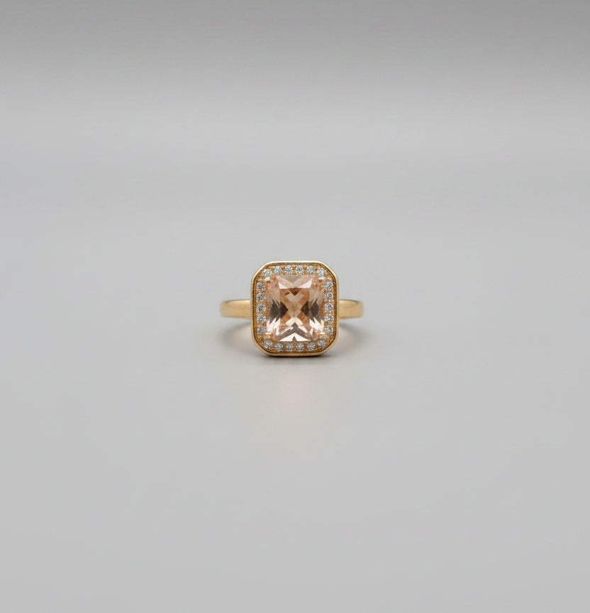 Gold ring with a large orange gemstone on a reflective surface
