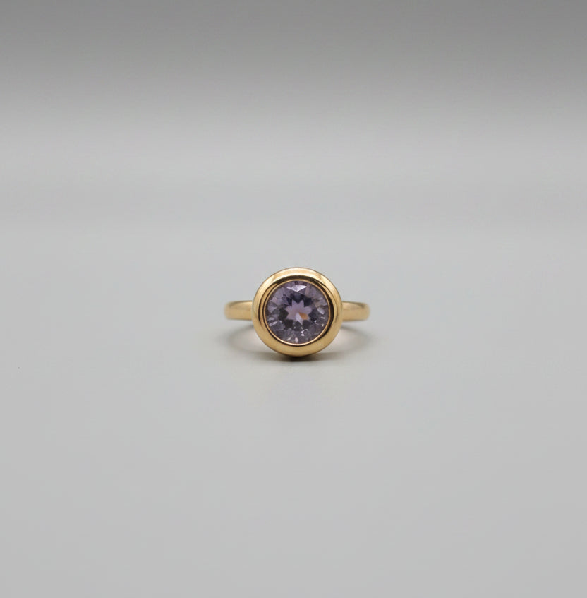 Gold ring with a central stone on a reflective surface