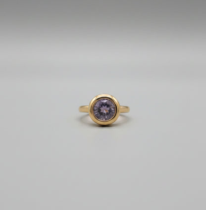 Gold ring with a central stone on a reflective surface