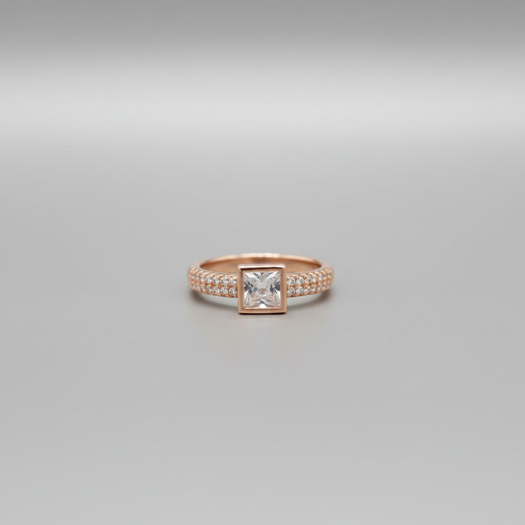 Gold ring with a square stone on a reflective surface