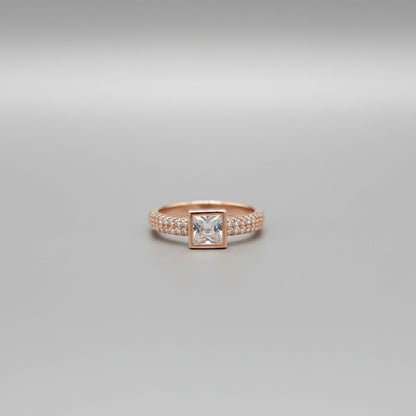 Gold ring with a square stone on a reflective surface