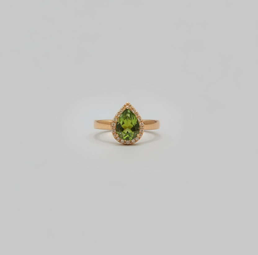 Gold ring with green gemstone on a reflective surface, blurred background