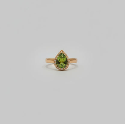 Gold ring with green gemstone on a reflective surface, blurred background