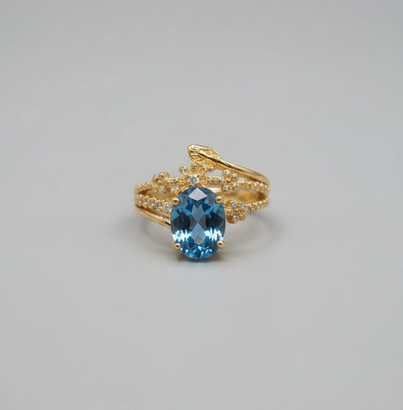 Gold ring with a blue gemstone on a reflective surface