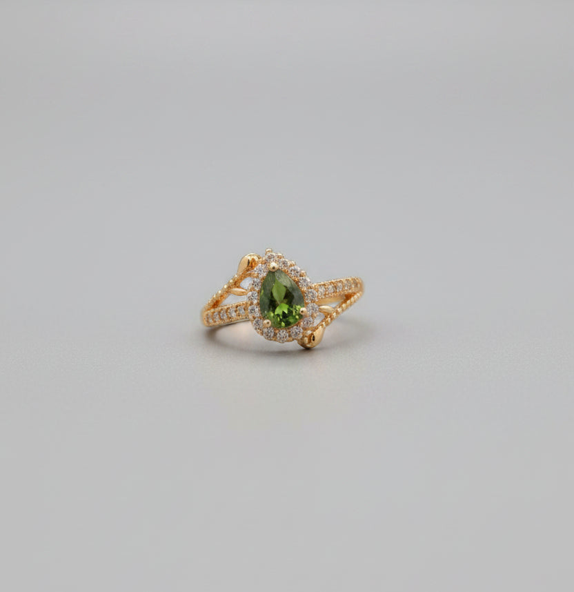 Gold ring with green gemstone on a reflective surface