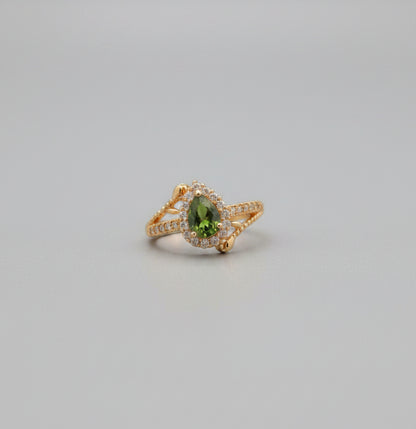 Gold ring with green gemstone on a reflective surface