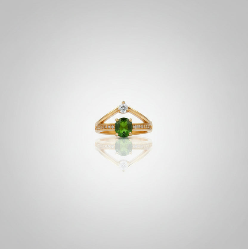 Gold ring with a green gemstone on a reflective surface, blurred background