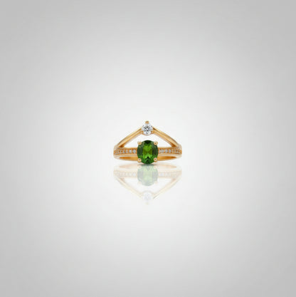 Gold ring with a green gemstone on a reflective surface, blurred background