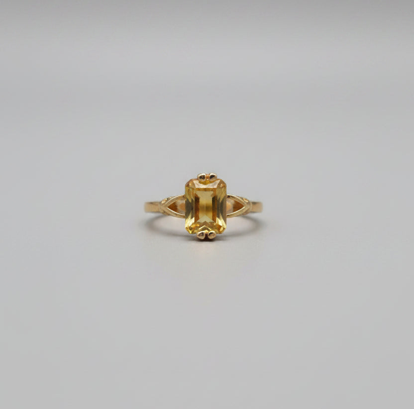 Gold ring with a large central stone on a reflective surface