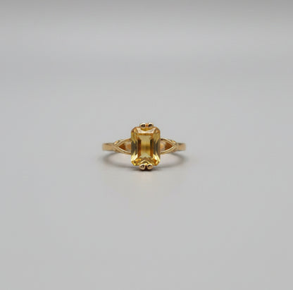 Gold ring with a large central stone on a reflective surface