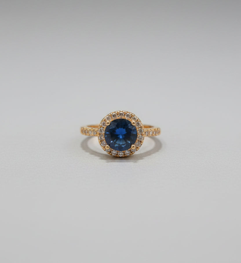 Gold ring with a blue gemstone on a reflective surface