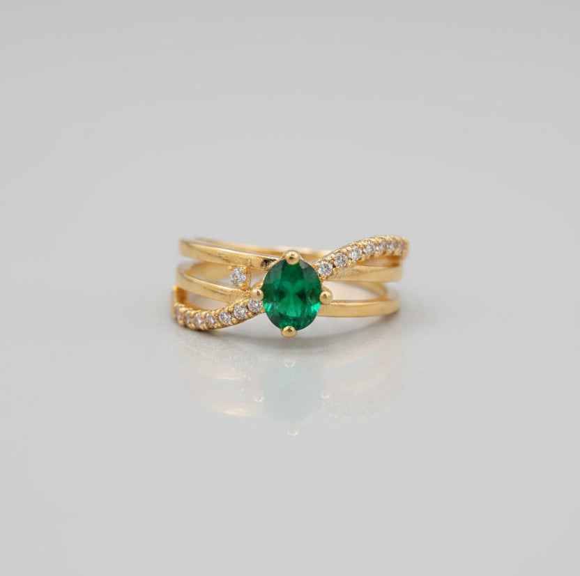 Gold ring with a green gemstone on a reflective surface
