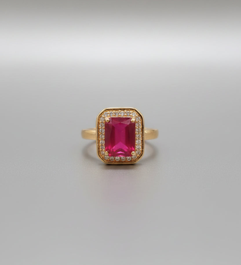 Gold ring with a red gemstone on a reflective surface
