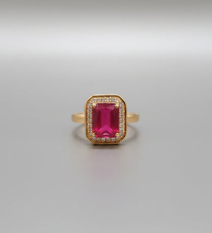 Gold ring with a red gemstone on a reflective surface