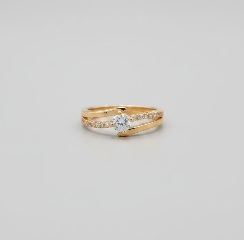 Gold ring with a clear gemstone on a reflective surface, blurred background