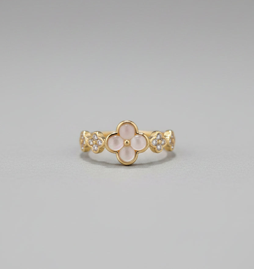 Gold ring with floral design on a reflective surface, blurred background