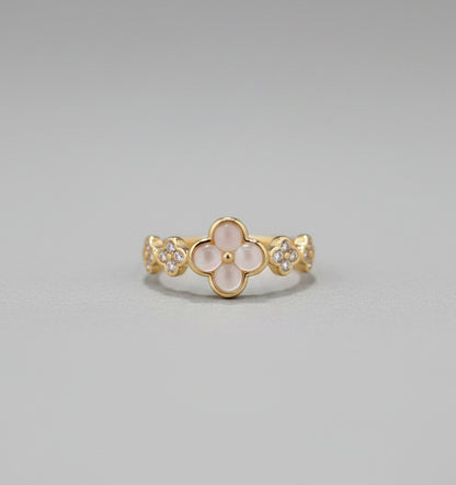 Gold ring with floral design on a reflective surface, blurred background