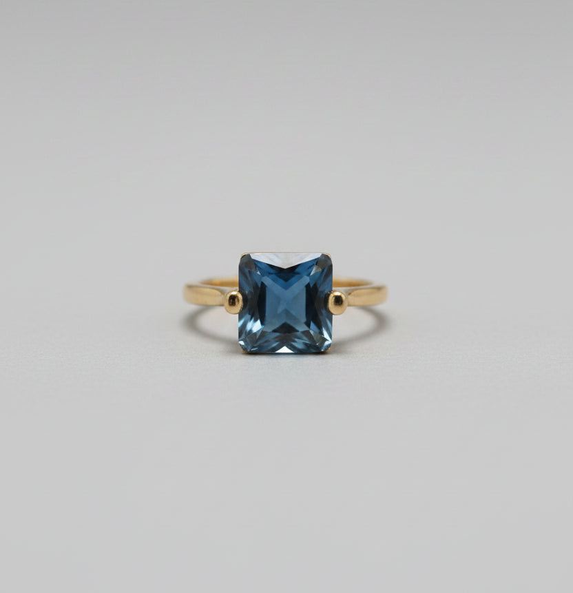 Gold ring with a blue gemstone on a blurred background