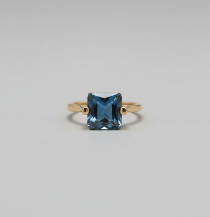 Gold ring with a blue gemstone on a blurred background
