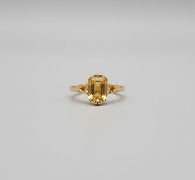 Gold ring with a yellow gemstone on a reflective surface, blurred background