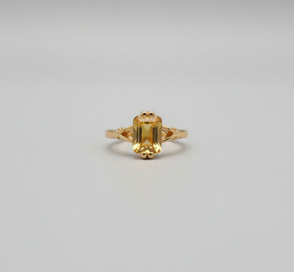 Gold ring with a yellow gemstone on a reflective surface, blurred background