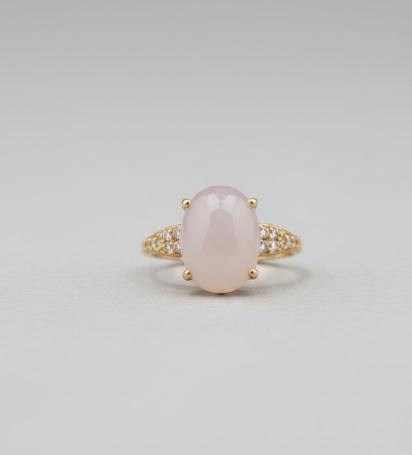 Gold ring with a large central stone on a reflective surface