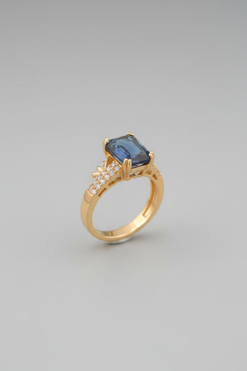 Gold ring with a blue gemstone on a reflective surface, blurred background