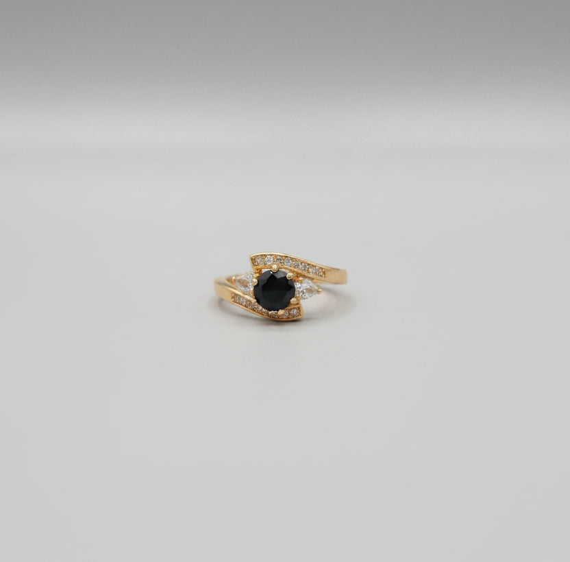 Gold ring with a black gemstone on a reflective surface
