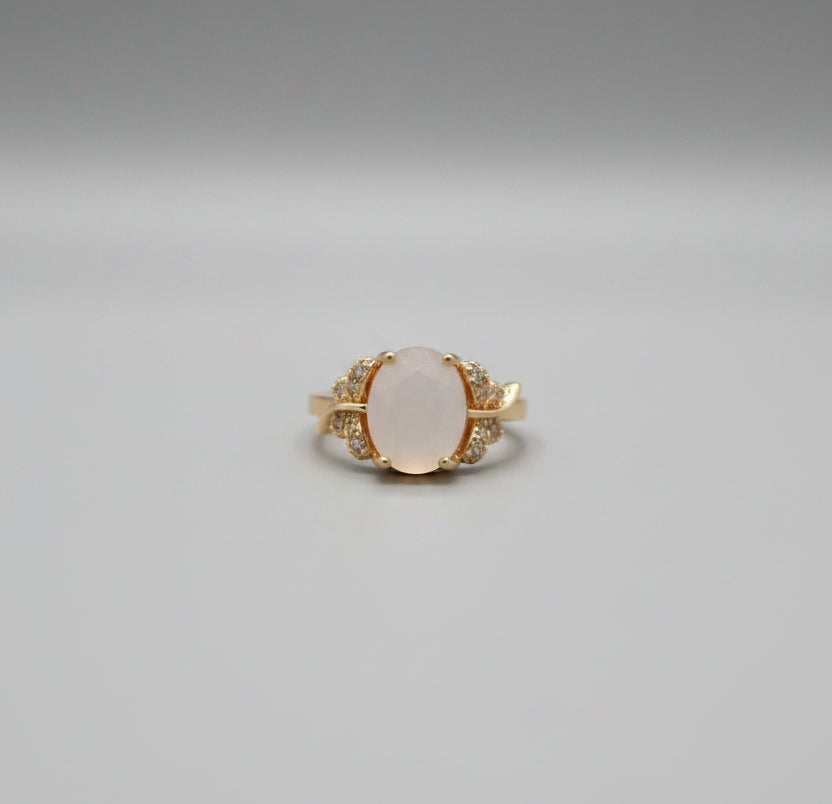 Gold ring with a central stone on a reflective surface, blurred background