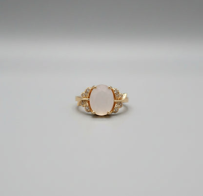 Gold ring with a central stone on a reflective surface, blurred background