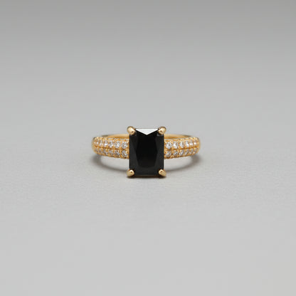 Gold ring with a black gemstone on a reflective surface