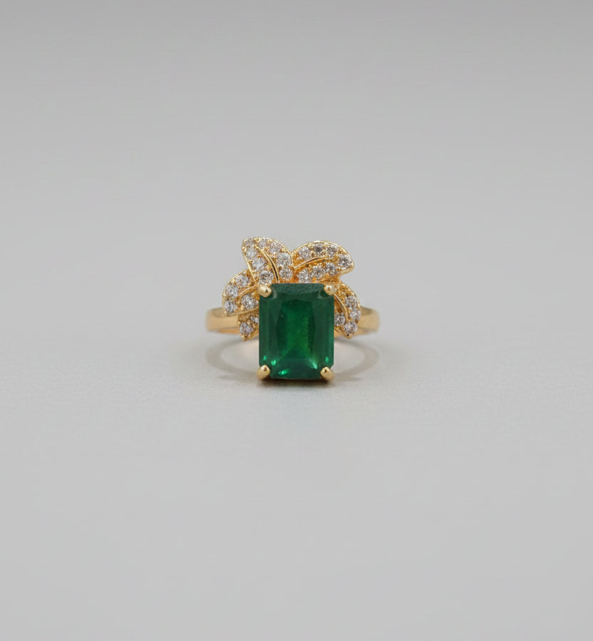 Gold ring with a green gemstone on a reflective surface