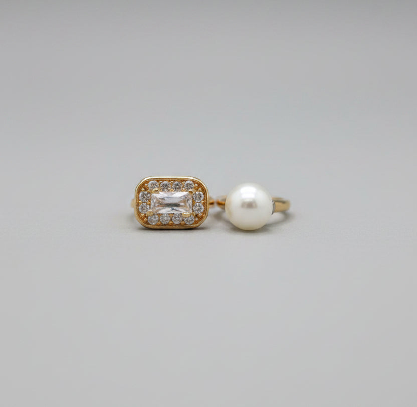 Two rings, one gold and one pearl, on a reflective surface with a blurred background.
