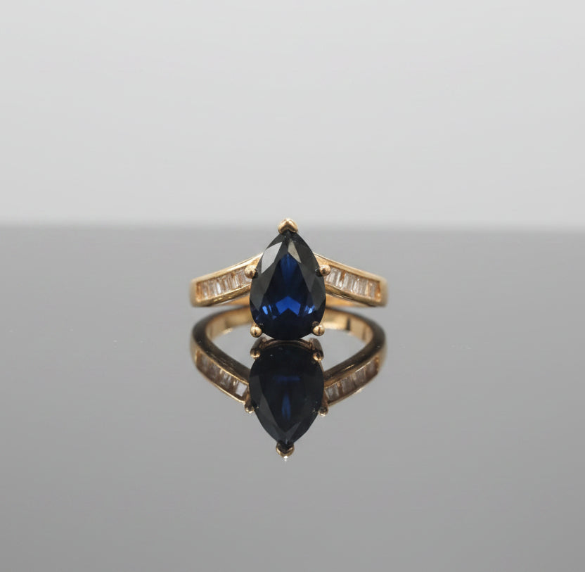 Gold ring with a black gemstone on a reflective surface