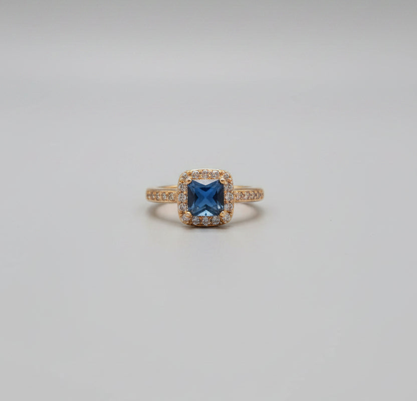 Gold ring with a blue gemstone on a reflective surface